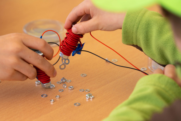 Zwei Kinder experimentieren mit selbstgebauten Elektromagneten und kleinen Metallscheiben auf einem Tisch.