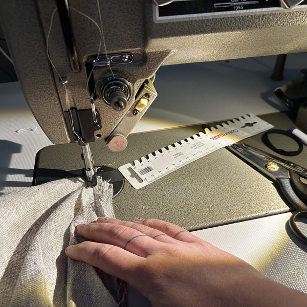 Eine Hand führt ein Textil unter eine Nähmaschine
